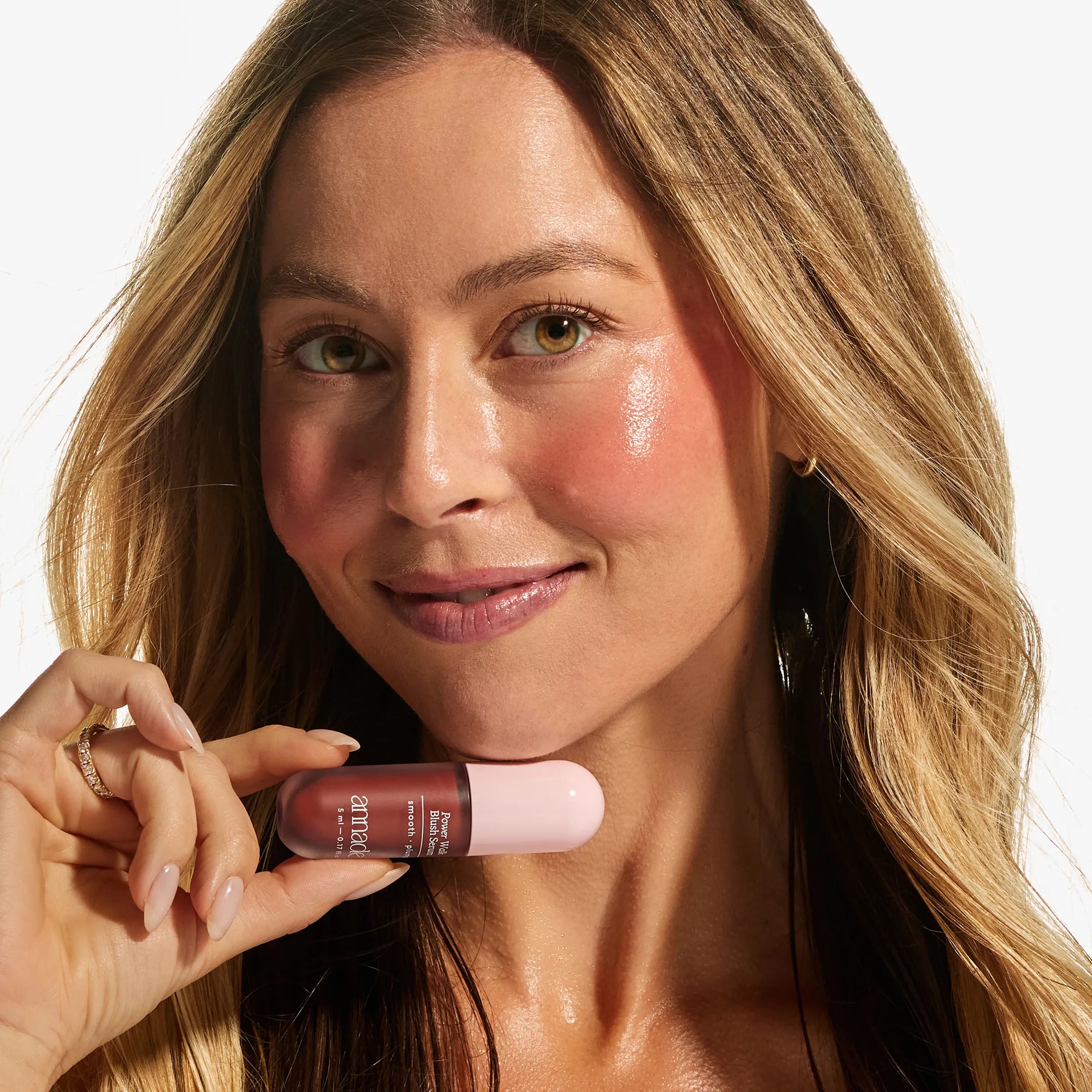Model with light skin tone holding the Annadea Power Walk Blush Serum in Late Date, showing a warm bronzed terracotta flush across the cheeks and a natural dewy finish from the hydrating blush serum