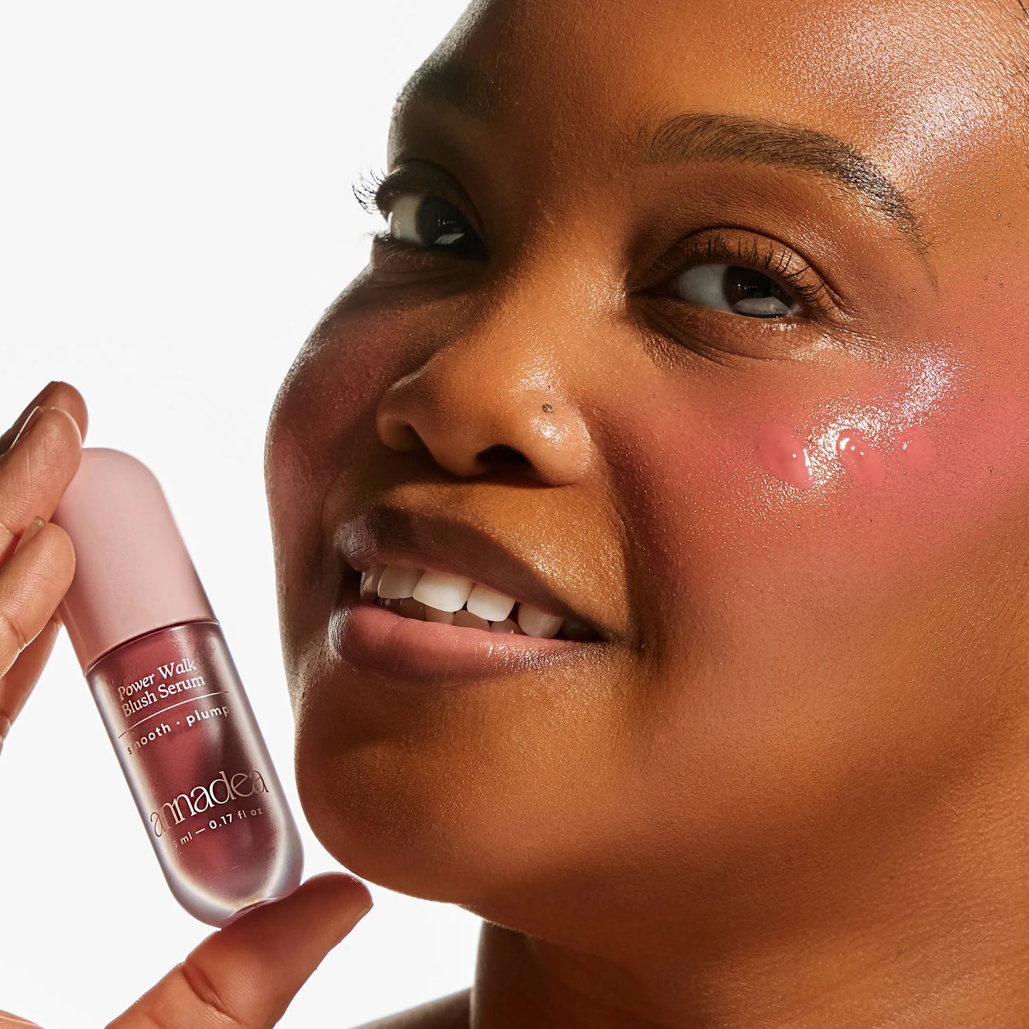 Close-up of a model with deep skin tone holding the Annadea Power Walk Blush Serum in Rose Trail, showing a vibrant rose flush and luminous dewy finish from the hydrating blush serum