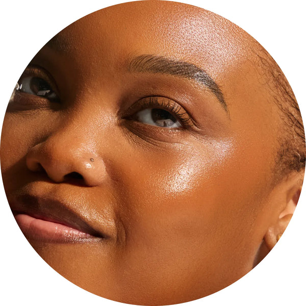 Close-up circular crop of a model with deep skin tone showing radiant, supple skin from the Annadea To Dew Glow Serum, highlighting the serum's nourishing glow and skin-strengthening results