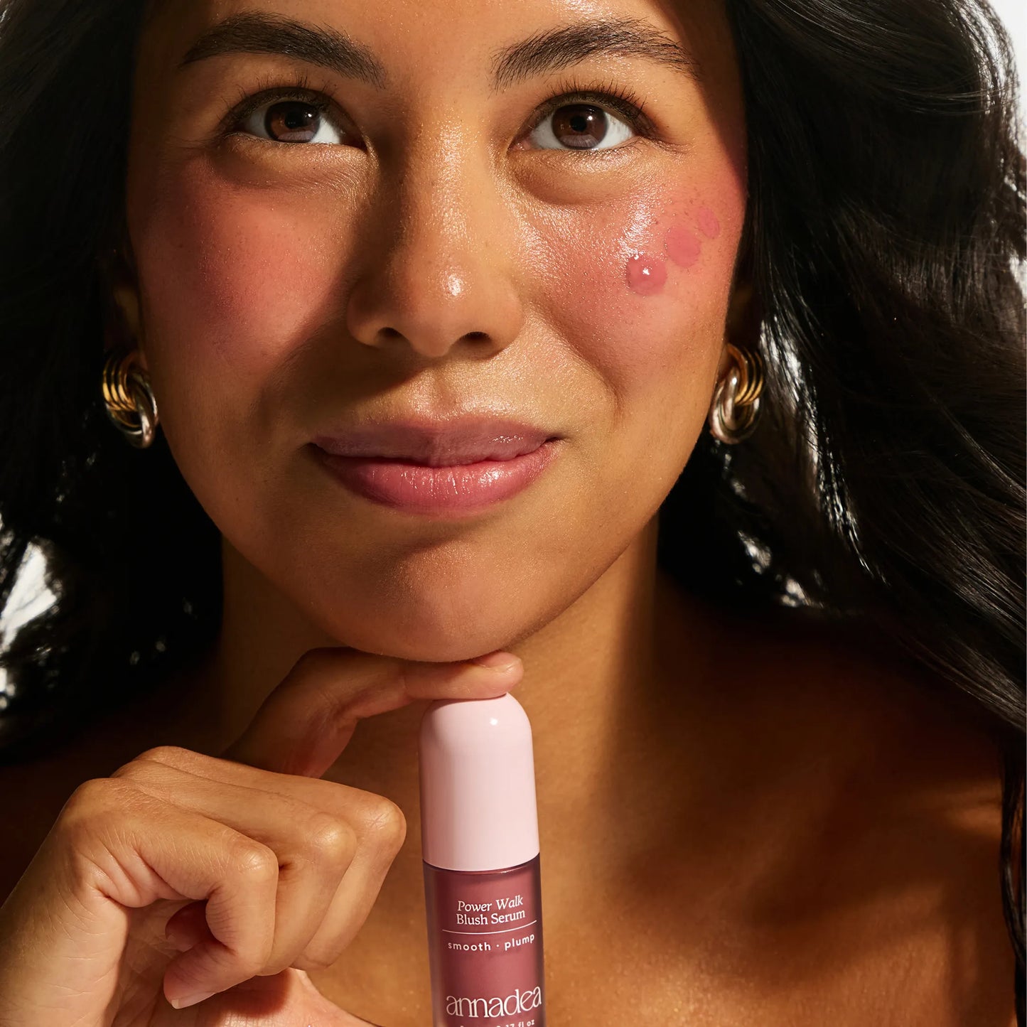 Model with medium skin tone showing Annadea Power Walk Blush Serum in Rose Trail dotted on cheeks before blending, demonstrating the serum application technique for a natural buildable flush