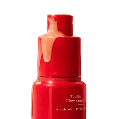 Close-up of the Annadea To Dew Glow Serum pump top with amber serum dripping down the red bottle, showing the lightweight gel texture of the brightening serum