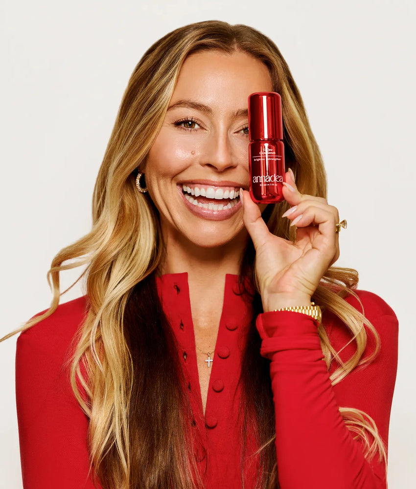 Annadea Co-Founder and CEO Olivia Adriance smiling and holding the To Dew Glow Serum in a red bottle against her cheek