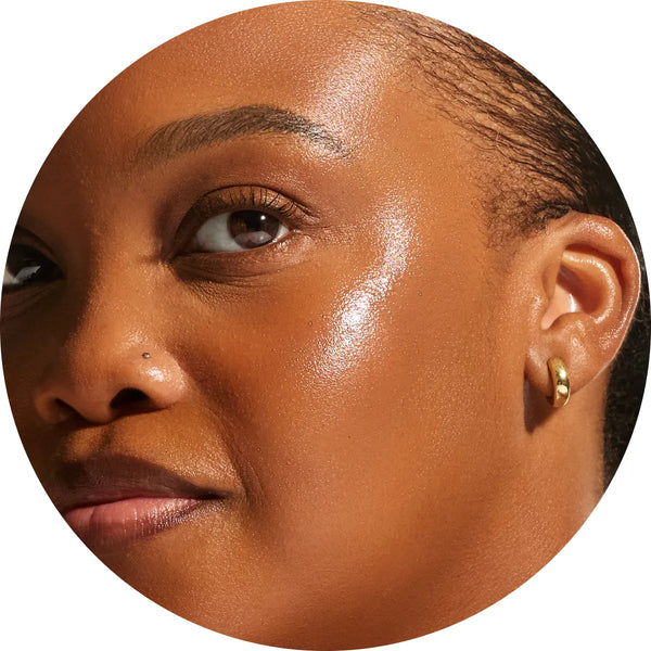 Close-up circular crop of a model with deep skin tone showing naturally toasted, luminous skin from the Annadea PTO Glow Bronzing Serum, reflecting the serum's warm sun-kissed bronzing finish