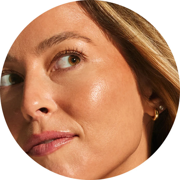 Close-up circular crop of a model with light skin tone showing warm, sun-kissed radiance from the Annadea PTO Glow Bronzing Serum, highlighting the serum's naturally toasted luminous finish free of glitter or orange tones