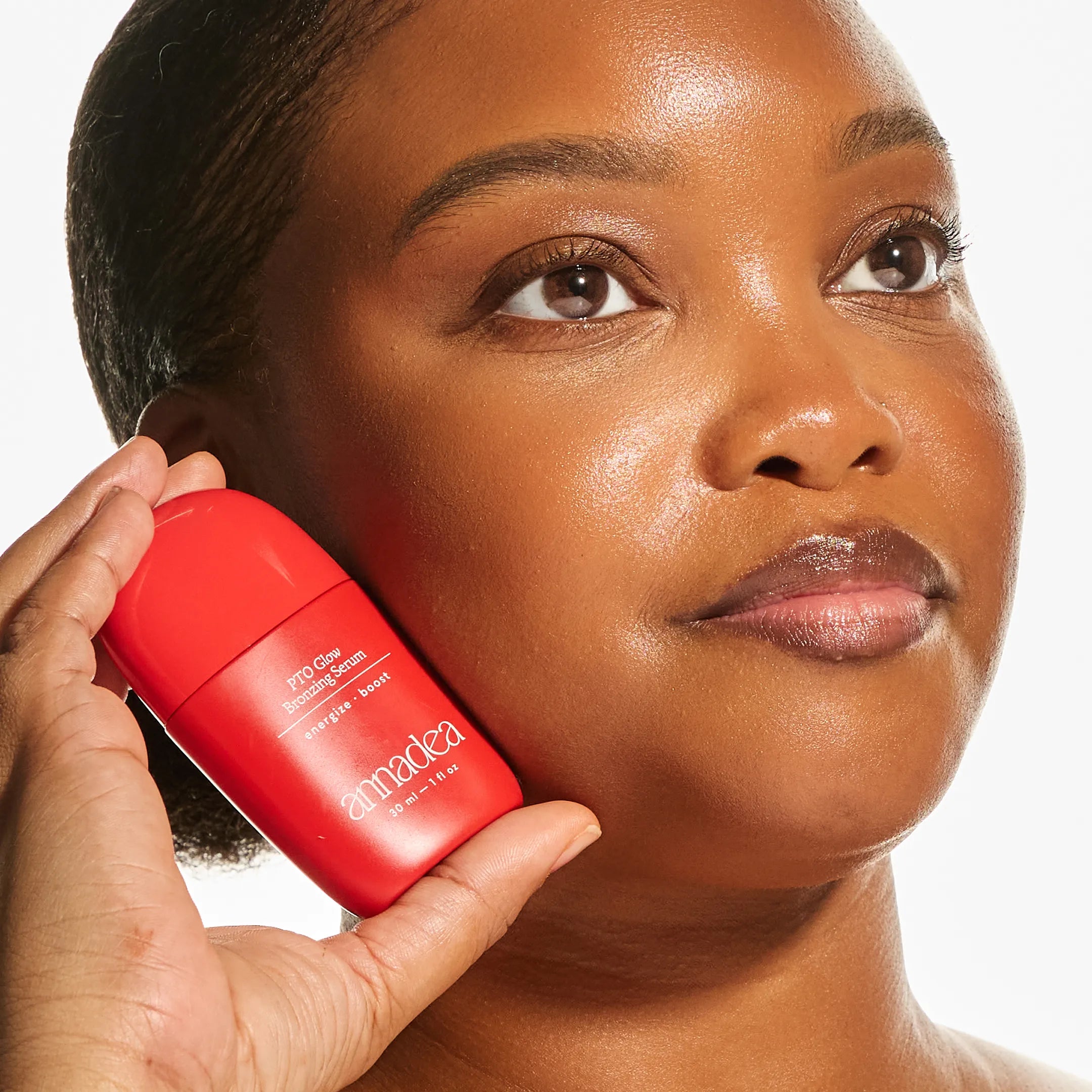 Model with deep skin tone holding the Annadea PTO Glow Bronzing Serum against her cheek, highlighting the serum's naturally toasted, luminous bronzing finish and skin-nourishing results