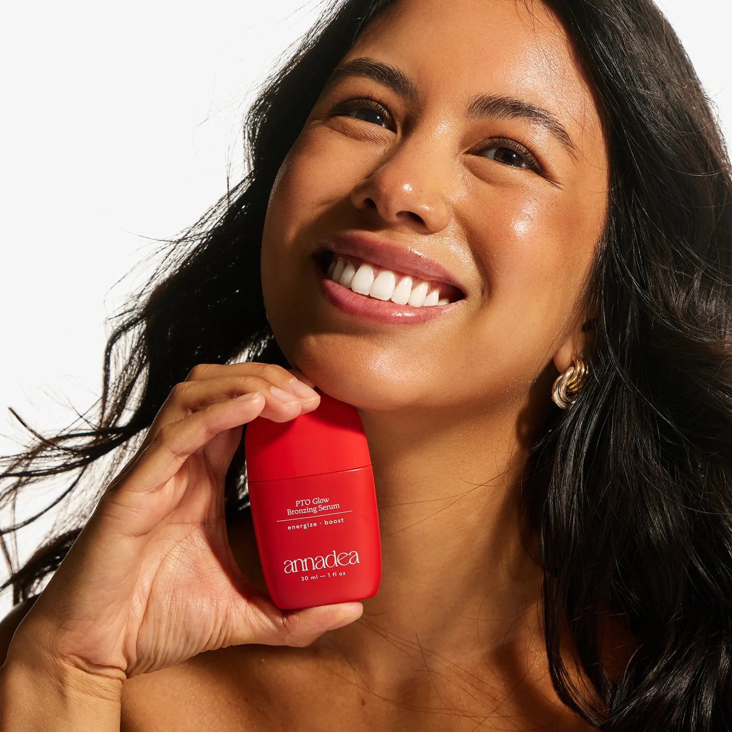 Smiling model with glowing medium skin tone holding the Annadea PTO Glow Bronzing Serum, reflecting the serum's buildable sun-kissed warmth and luminous bronzing finish