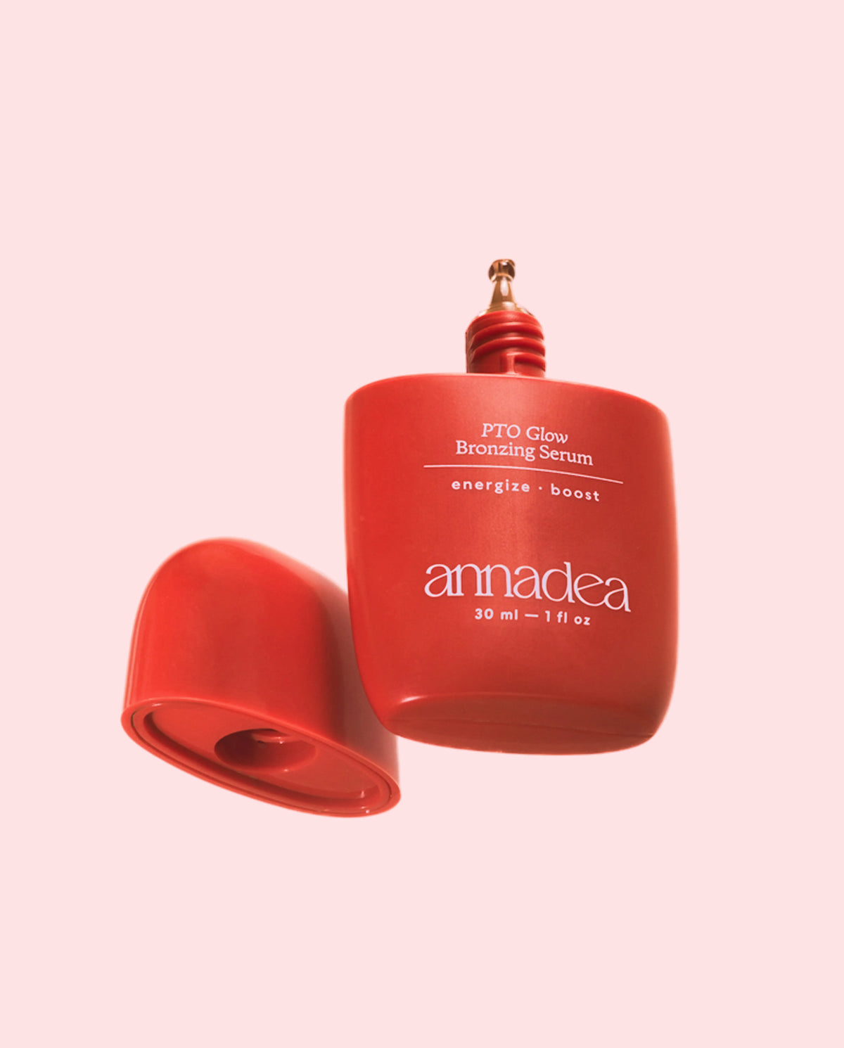 Annadea PTO Glow Bronzing Serum matte red bottle with cap removed revealing the bronze applicator tip, photographed on a soft pink background showing the energize and boost bronzing serum