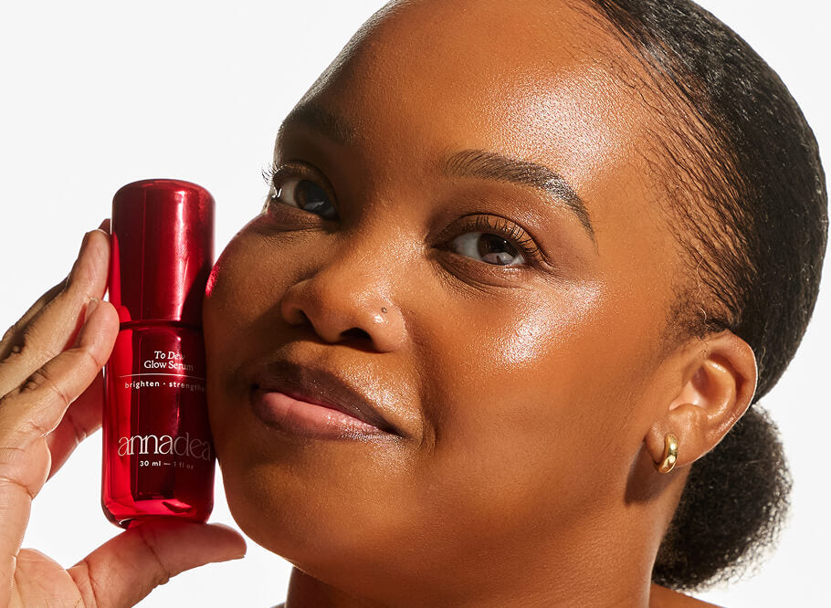 Model with deep skin tone holding the Annadea To Dew Glow Serum close to her cheek, showing a brightened, hydrated complexion